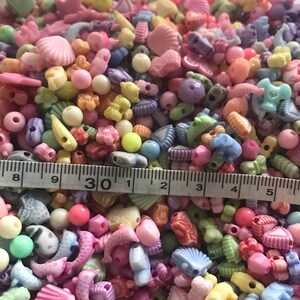 May include: A large assortment of colorful plastic beads in various shapes, including shells, hearts, stars, and dolphins. The beads are approximately 1/2 inch in size and are perfect for crafting jewelry or other projects.