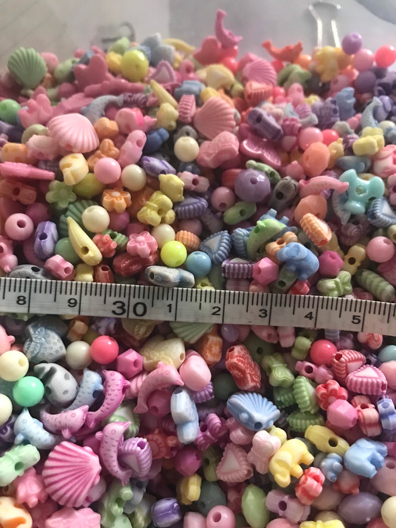 May include: A large assortment of colorful plastic beads in various shapes, including shells, hearts, stars, and dolphins. The beads are approximately 1/2 inch in size and are perfect for crafting jewelry or other projects.