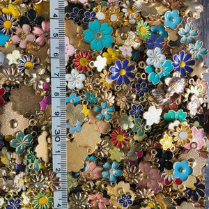 Puede incluir: Un gran surtido de abalorios de flores de esmalte de colores con engastes de metal dorado. Los abalorios est&aacute;n esparcidos sobre una superficie con una regla en el fondo.