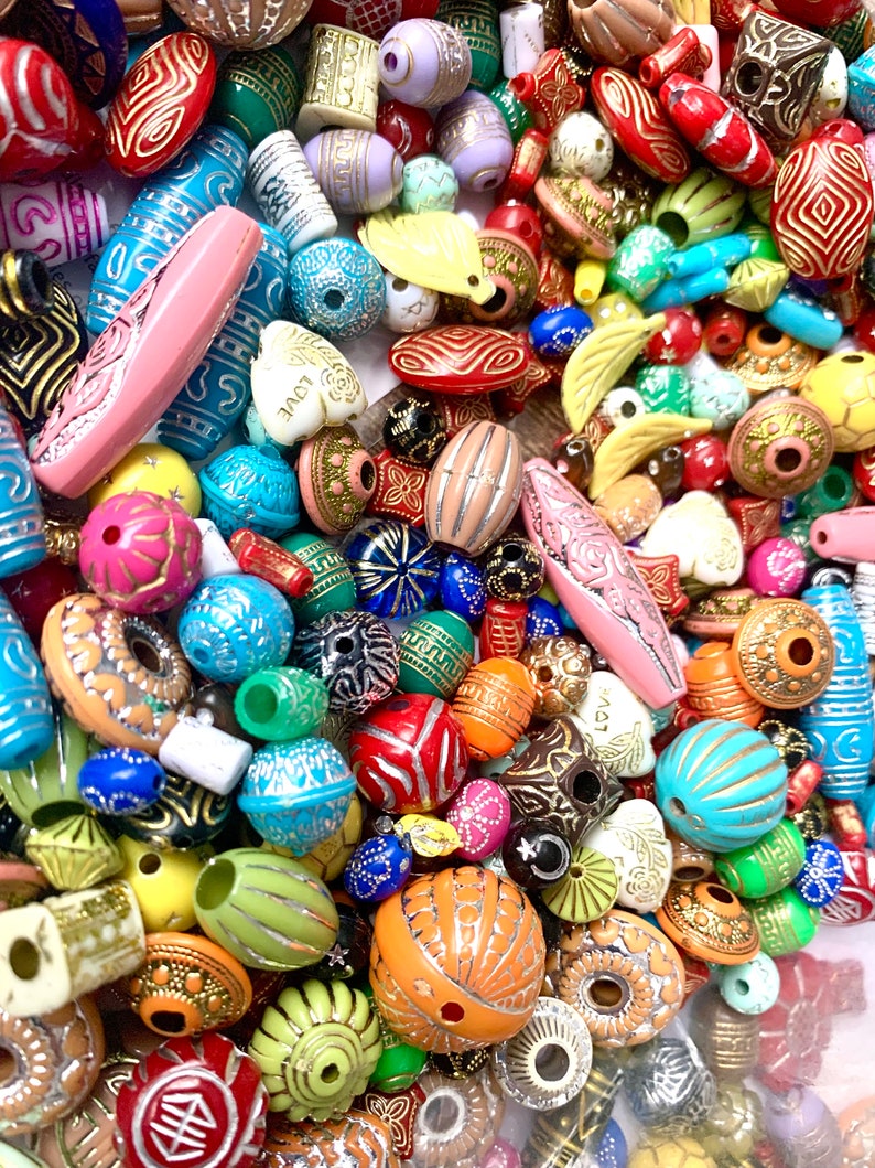 May include: A large assortment of colorful, patterned beads. The beads are made of various materials, including wood, plastic, and glass. They are all different shapes and sizes, and some have metallic accents. The beads are perfect for making jewelry, crafts, and other projects.