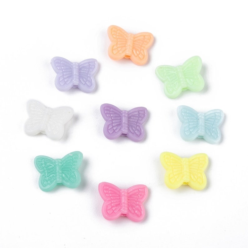 Op de afbeelding: Assortiment van tien pastelkleurige plastic vlinder kralen. De kralen zijn in tinten paars, roze, blauw, groen, geel en oranje.