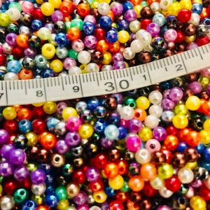 May include: A close-up image of a large assortment of colorful plastic beads. The beads are various shades of red, orange, yellow, green, blue, purple, pink, brown, black, and white. A white measuring tape is partially visible in the image, with the number "30" clearly visible.