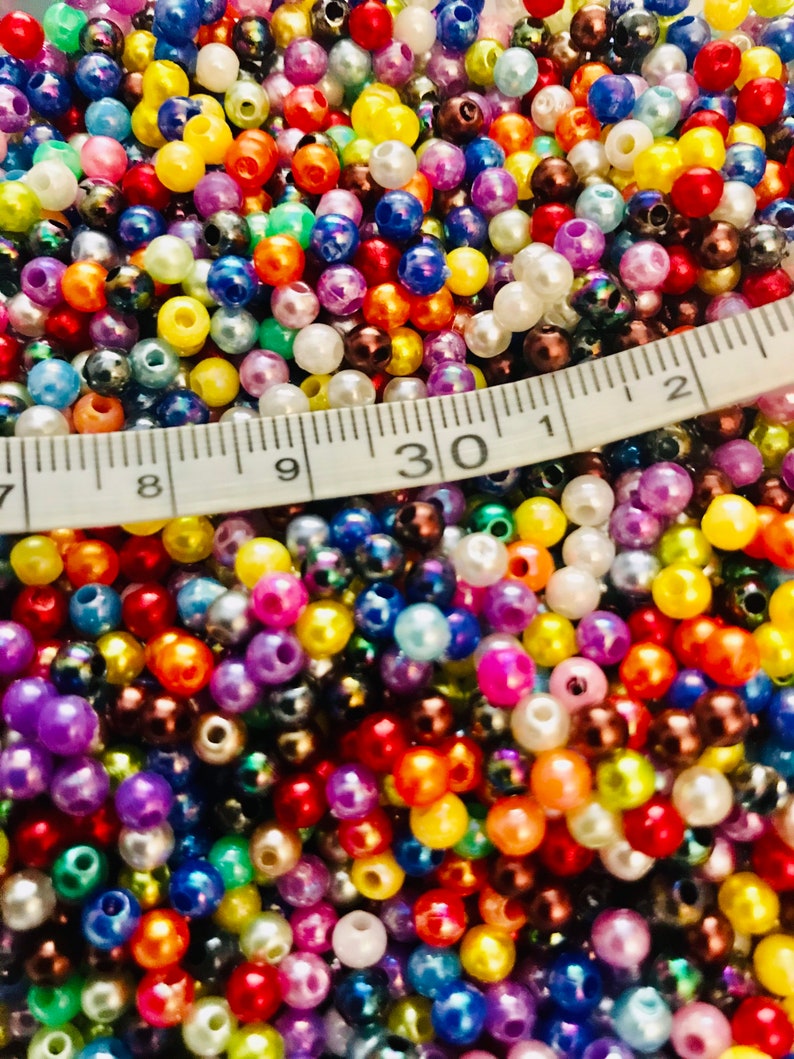 May include: A close-up image of a large assortment of colorful plastic beads. The beads are various shades of red, orange, yellow, green, blue, purple, pink, brown, black, and white. A white measuring tape is partially visible in the image, with the number "30" clearly visible.