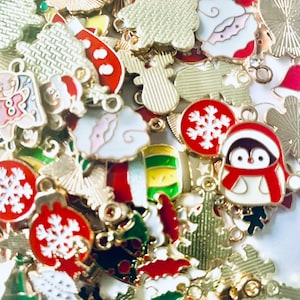 May include: Assortment of gold-tone metal Christmas charms with enamel details. Charms include a snowman, a penguin, a Christmas tree, a snowflake, and a stocking.