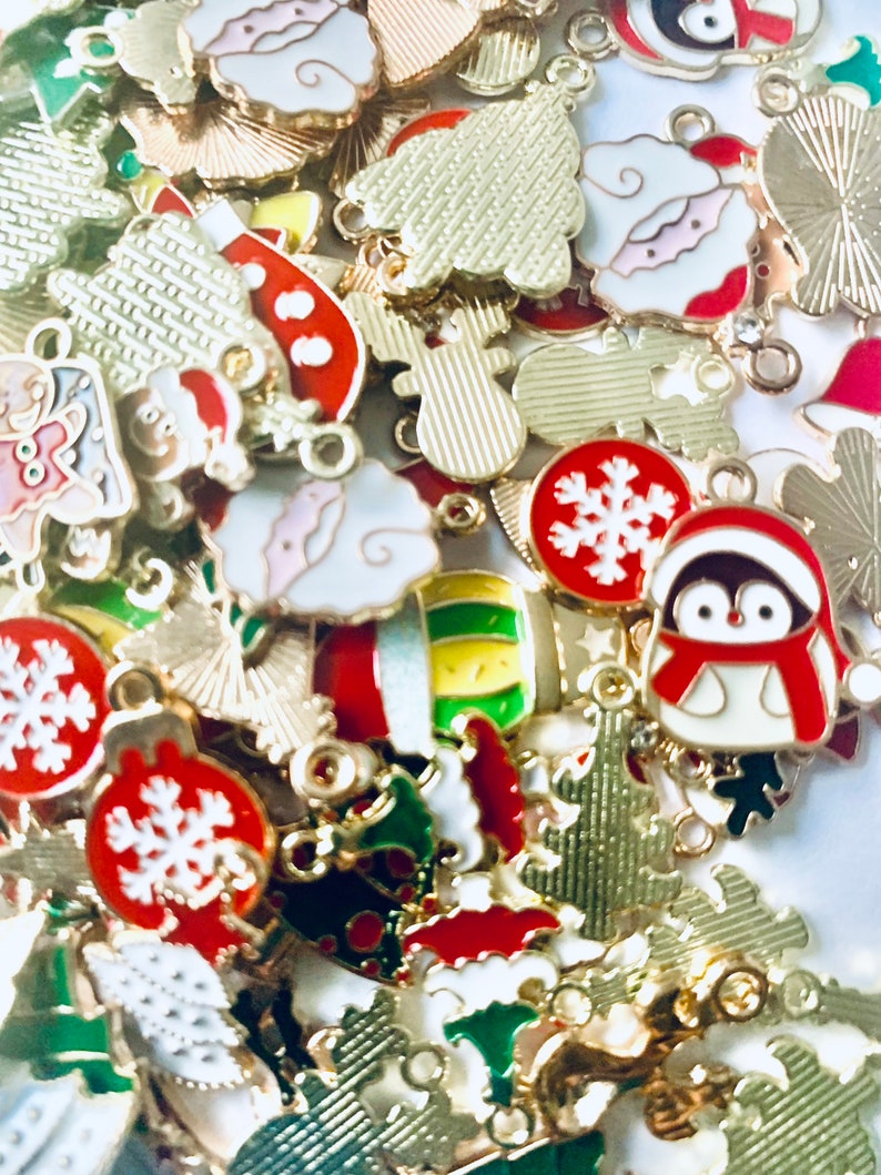 May include: Assortment of gold-tone metal Christmas charms with enamel details. Charms include a snowman, a penguin, a Christmas tree, a snowflake, and a stocking.