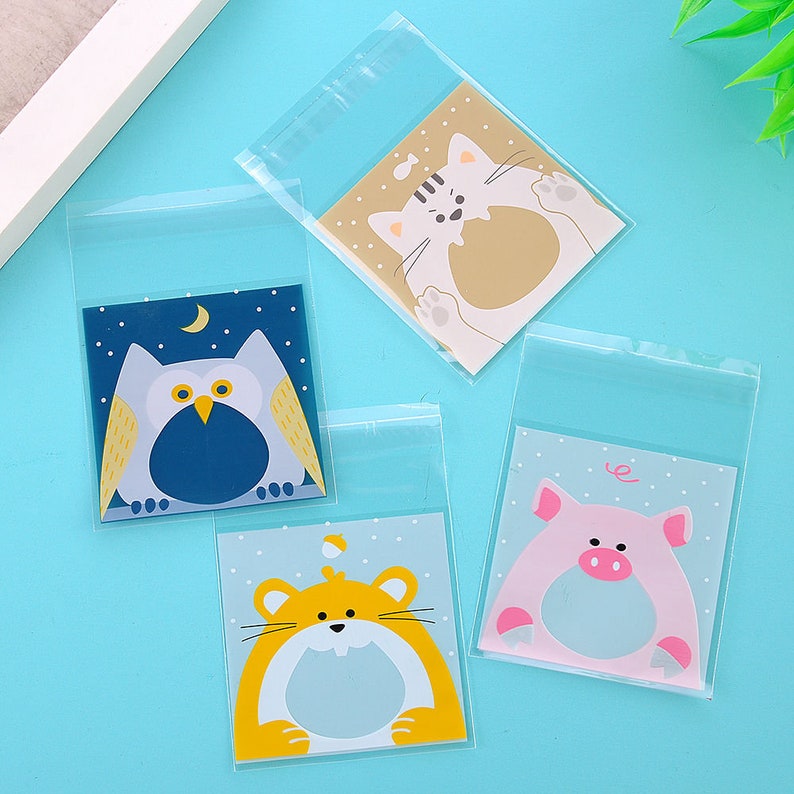 May include: Four clear plastic bags with different animal designs. The bags have a white background with a blue, yellow, pink, or brown animal on each. The animals are an owl, a hamster, a pig, and a cat.