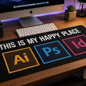 May include: A rectangular black desk mat featuring the white text "THIS IS MY HAPPY PLACE" and three colorful square icons representing software applications with the letters "Ai" in yellow, "Ps" in blue, and "Id" in pink on a dark background.