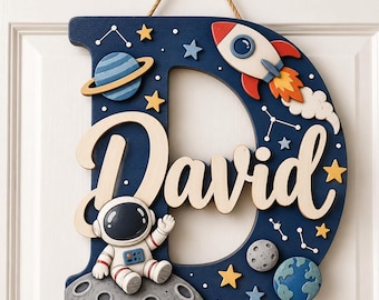 May include: A dark blue wooden letter D wall hanging featuring the name David in script lettering. The design includes a space theme with a rocket ship, an astronaut on a moon surface, a planet with rings, Earth, stars, and white constellation lines.