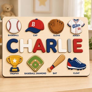 Könnte beinhalten: Ein Holz-Namenspuzzle mit dem Namen CHARLIE in großen, bunten Buchstaben. Um den Namen herum befinden sich acht Puzzleteile zum Thema Baseball: ein Baseball, eine Kappe, ein Handschuh, ein Trikot, ein Pokal, ein Spielfeld, ein Schläger und ein Schuh.