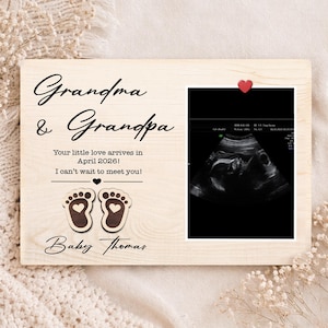 Puede incluir: Un marco de fotos de madera con las palabras "Grandma & Grandpa" y "Baby Thomas" en escritura negra. El marco incluye una imagen de ultrasonido y el texto "Your little love arrives in April 2026! I can't wait to meet you!"