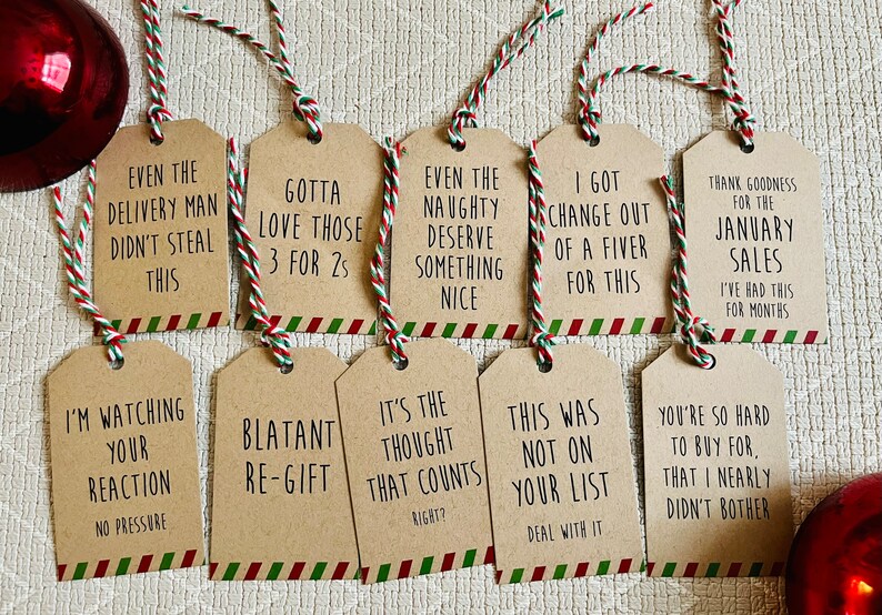May include: Ten brown gift tags with red and green striped borders and twine. The tags have humorous sayings on them, such as "Even the delivery man didn't steal this" and "I'm watching your reaction, no pressure".