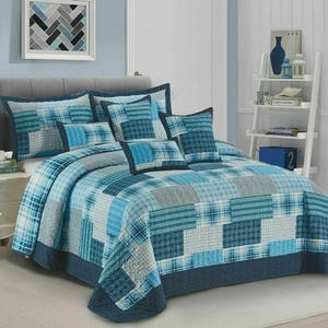 May include: A bed dressed with a blue and grey patchwork quilt set. The quilt and matching pillows feature a variety of square and rectangular patterns. The colour scheme is mainly shades of blue and grey.