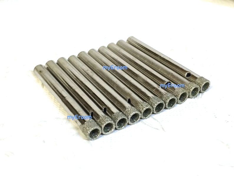 May include: A collection of ten silver-colored diamond-tipped drill bits. Each bit has a cylindrical body and a textured, diamond-coated tip for drilling into hard materials. The bits are arranged on a white surface.