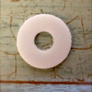 May include: A white felt circle with a hole in the centre. The circle is approximately 5 cm in diameter.