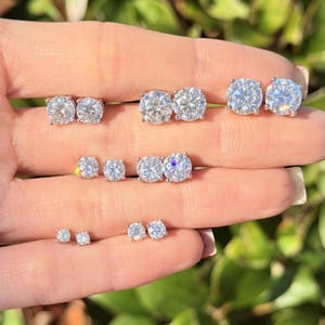 May include: A collection of sparkling diamond stud earrings in various sizes. The earrings are round-cut and set in a silver or white metal. The image shows multiple pairs of earrings, showcasing their brilliance and clarity.