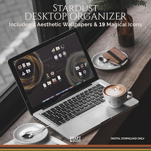 May include: A laptop displays a desktop organizer with a dark background and swirling designs. The screen shows icons and two aesthetic wallpapers. A cup of coffee, a small plate with a spoon, and a coaster are on the table. Text on the screen reads "STARDUST DESKTOP ORGANIZER".