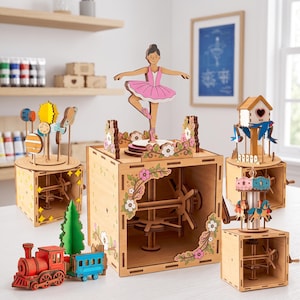 Puede incluir: Una colección de cinco cajas de música mecánicas de madera que incluyen una bailarina sobre una base floral, un modelo del sistema solar, una pajarera con pájaros azules, un carrusel con caballos y un tren rojo y azul con un árbol verde.