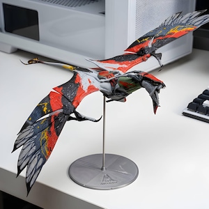 May include: A detailed action figure of a flying creature with large, outstretched wings featuring a vibrant pattern of black, red, and yellow. The creature has a long tail, a sharp-toothed open mouth, and is mounted on a silver metal display stand.