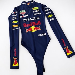 May include: Navy blue bodysuit with long sleeves, featuring multiple sponsor logos and the Red Bull logo. The bodysuit has a high neckline and a form-fitting design. The text "zoom" is visible on the neckline.