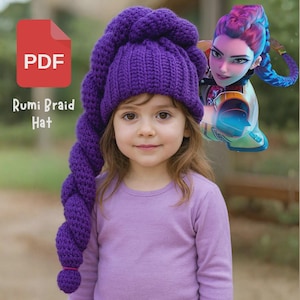 May include: A young girl wearing a vibrant purple crochet hat with a long, braided tail. The hat is labeled "Rumi Braid Hat" with a PDF icon. The girl is wearing a purple long-sleeve shirt. A cartoon character is in the background.