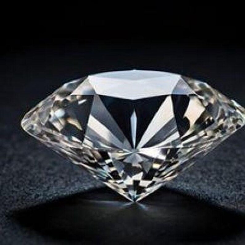 May include: A clear, colorless, round brilliant-cut diamond featuring numerous triangular and kite-shaped facets that reflect light to create sharp, geometric patterns. The gemstone has a pointed culet at the base and a wide, flat table top.