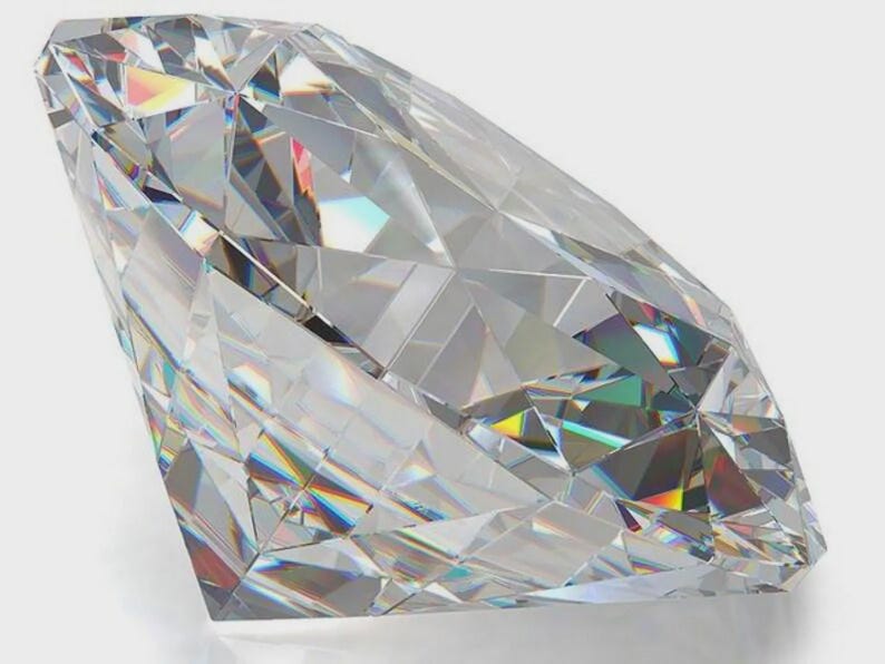 May include: A clear, colorless, faceted gemstone with a brilliant cut. The stone features numerous triangular and kite-shaped facets that reflect light, creating internal prismatic rainbow refractions and sharp geometric edges throughout.