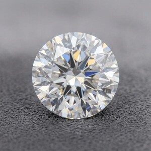 May include: A round brilliant cut gemstone with a clear, colorless appearance and multiple triangular and kite-shaped facets that create a high level of light reflection and sparkle throughout the entire surface of the stone.