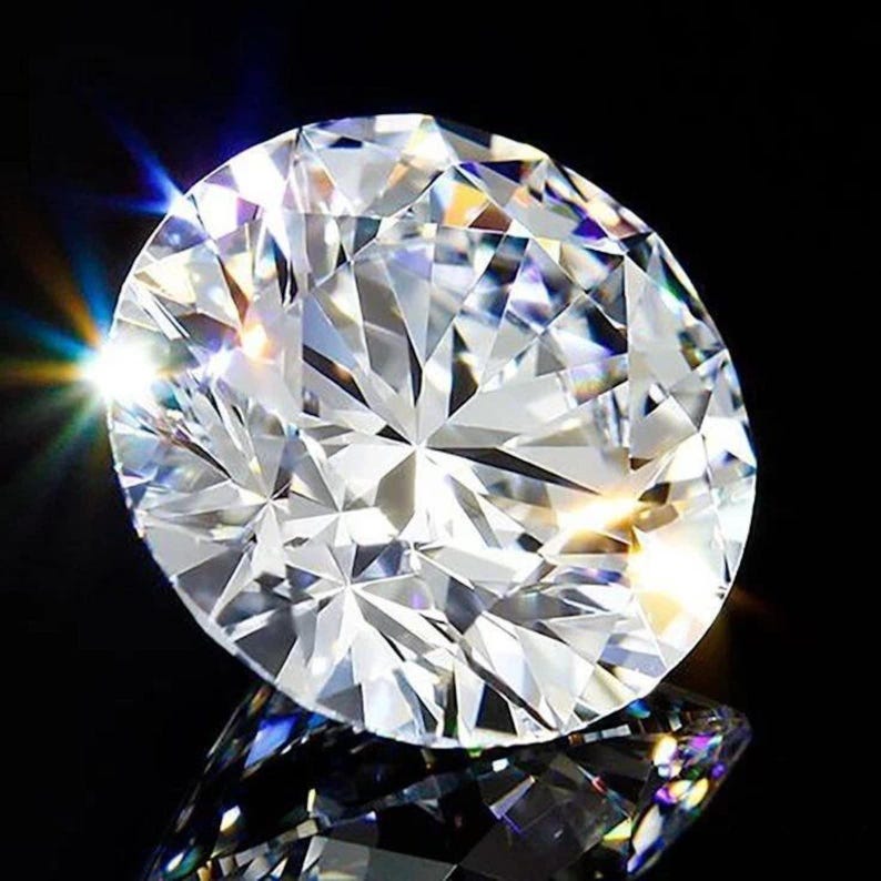May include: A round brilliant cut diamond with numerous triangular and kite-shaped facets. The gemstone is clear and colorless, reflecting bright white light with sharp prismatic rainbow flares visible along the edges against a black background.