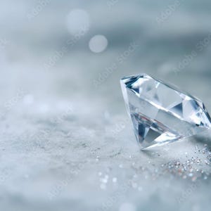 May include: A clear, faceted diamond gemstone with a brilliant cut, reflecting light with sharp edges and multiple triangular surfaces, resting on a cool-toned, textured surface with scattered shimmering particles surrounding the base.
