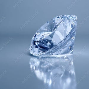 May include: A clear, faceted gemstone with a brilliant cut, displaying sharp geometric angles and light refraction. The stone is transparent and colorless, resting on a smooth, reflective surface that creates a distinct mirror image below it.