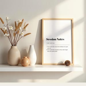 Puede incluir: Una impresión enmarcada con el texto "Session Notes" y una definición. La impresión se muestra en un estante blanco, junto a un jarrón beige con flores blancas, un jarrón blanco y un jarrón naranja pequeño. Una piña decorativa también está en el estante.