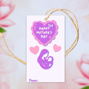 Puede incluir: Una etiqueta de regalo blanca con un dise&ntilde;o en forma de coraz&oacute;n p&uacute;rpura que dice "1st Happy Mother's Day". Debajo del coraz&oacute;n hay una silueta p&uacute;rpura de una madre sosteniendo a un beb&eacute;. Dos corazones rosas tambi&eacute;n est&aacute;n en la etiqueta. Una cuerda de hilo est&aacute; adjunta.