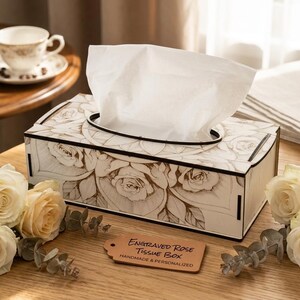 May include: A wooden tissue box with an engraved rose design, holding white tissues. The box is rectangular with a black rim and is accompanied by fresh roses and a tag that reads "Engraved Rose Tissue Box".