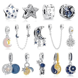 May include: A collection of silver-toned charms with celestial themes. The charms include stars, moons, and suns, some adorned with clear and blue gemstones. Several charms dangle from a chain or have a circular design.