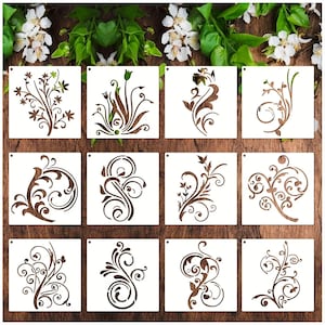 May include: A collection of twelve square stencils featuring various floral and botanical designs. Each stencil is a light brown color and has a different intricate pattern of leaves, vines, and flowers. The stencils are arranged on a wooden surface.