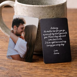 Op de afbeelding: Een keramische mok met een lichtbruine, gespikkelde afwerking, naast twee rechthoekige kaarten. Eén kaart heeft een foto van een stel dat elkaar omhelst. De andere is zwart met witte handgeschreven tekst: "Anthony, No matter how far you go...Love, Jenna."