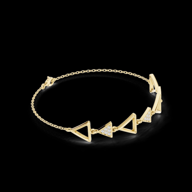 May include: A gold-colored bracelet with a delicate chain and geometric triangle design. The triangles are evenly spaced and some are embellished with small, sparkling stones. The bracelet is set against a black background.