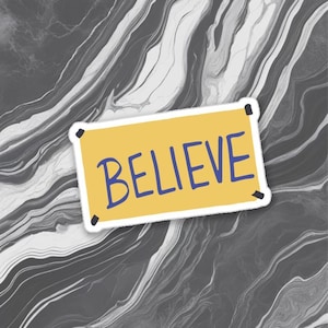 Puede incluir: Una pegatina amarilla con la palabra "BELIEVE" en letras azules. La pegatina es rectangular con esquinas redondeadas y detalles negros en las esquinas. El fondo es un patrón arremolinado de gris y blanco.