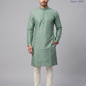 May include: A sage green long-sleeved kurta featuring a mandarin collar, a button-down placket, and a chevron pattern embellished with small circular mirrors. The garment is paired with off-white trousers and light-colored slip-on shoes.