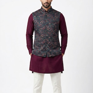 Pode incluir: Um conjunto masculino com um colete com estampa floral escura sobre uma camisa e túnica bordô de manga comprida. A roupa é completada com calças brancas. O colete tem gola mandarim.