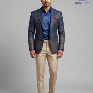 Puede incluir: Una americana azul marino con acabado texturizado, con un patrón de damasco marrón oscuro en los paneles inferiores y mangas, combinada con una camisa azul lisa, pantalones beige y zapatos de hebilla de cuero marrón. Logo: Since 1976.