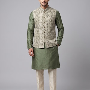 Könnte beinhalten: Ein olivgrüner, langärmeliger Kurta kombiniert mit einer cremefarbenen Hose und einer beigen, ärmellosen Weste mit dunklem geometrischem Muster. Die Weste hat einen Stehkragen und eine Knopfleiste vorne. Abgerundet wird das Outfit durch braune Lederschuhe.
