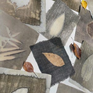 Pode incluir: Vista aérea de vários pedaços de tecido com impressões de folhas em tons de cinza, marrom e bege. Alguns tecidos têm bordas desfiadas. Folhas secas marrons e amarelas espalhadas.