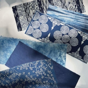Puede incluir: Una variedad de muestras de tela teñidas con índigo. Las telas presentan varios patrones, incluyendo diseños florales, geométricos y abstractos. La paleta de colores consiste en tonos de azul y blanco, creando una colección textil visualmente atractiva.