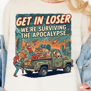 May include: A cream-coloured sweatshirt featuring a graphic illustration of a rusty green pickup truck loaded with supplies. The text reads GET IN LOSER WE'RE SURVIVING THE APOCALYPSE. The scene depicts people, a city skyline, and falling meteors.