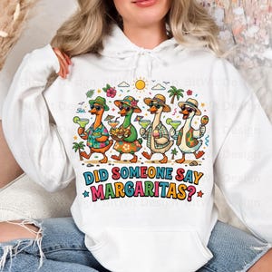 May include: A white hooded sweatshirt featuring a colorful graphic of four cartoon ducks wearing tropical hats and sunglasses, holding margaritas and snacks. The text below the ducks reads, "DID SOMEONE SAY MARGARITAS?" in bold, multi-colored letters.
