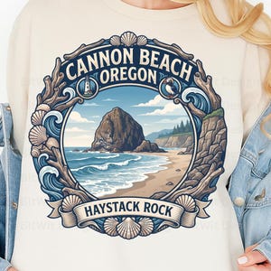 Könnte beinhalten: Ein cremefarbenes Sweatshirt mit einer kreisförmigen Grafik von Haystack Rock in Cannon Beach, Oregon. Das Design zeigt einen Leuchtturm, einen Papageientaucher, Meereswellen und Muscheln sowie den Text Cannon Beach Oregon und Haystack Rock.