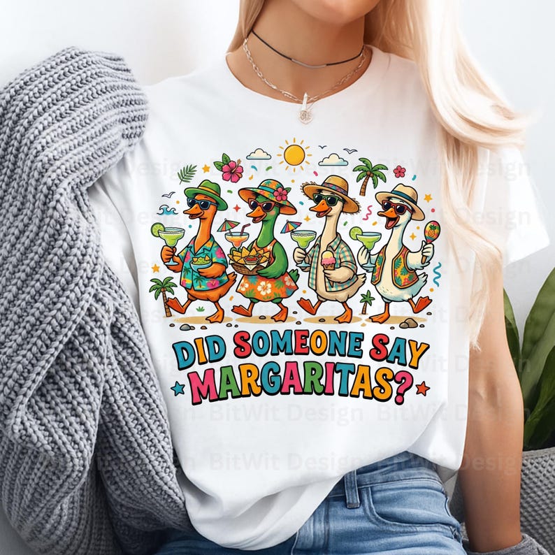 May include: A white t-shirt featuring a colorful graphic of four ducks wearing hats and sunglasses, holding margaritas and snacks under a sun and palm trees. The text below the ducks reads, DID SOMEONE SAY MARGARITAS? in bold, multi-colored letters.