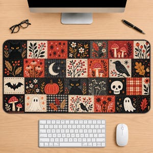 May include: A rectangular desk mat featuring a patchwork design of autumn and Halloween motifs including black cats, ghosts, skulls, pumpkins, bats, ravens, mushrooms, and floral patterns in a color palette of black, orange, red, and cream.