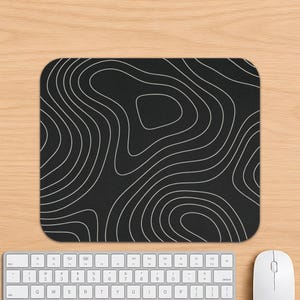 May include: A rectangular mouse pad featuring a black background with a white topographic map pattern consisting of continuous, flowing contour lines that create an abstract, layered effect across the entire surface of the rectangular mat.